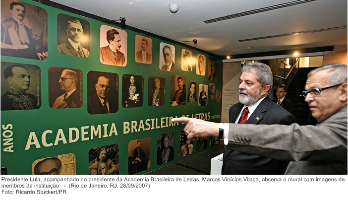 Presidente Lula, acompanhado do presidente da Academia Brasileira de Letras, Marcos Vinícios Vilaça, observa o mural com imagens de membros da instituição.