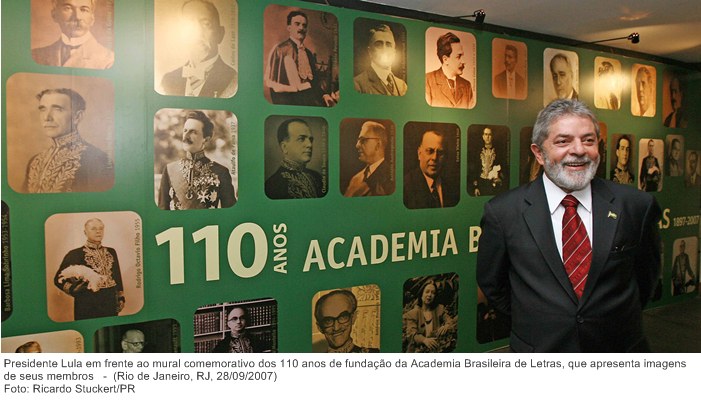 Presidente Lula em frente ao mural comemorativo dos 110 anos de fundação da Academia Brasileira de Letras, que apresenta imagens de seus membros.