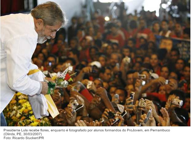 Presidente Lula recebe flores, enquanto é fotografado por alunos formandos do ProJovem, em Pernambuco.